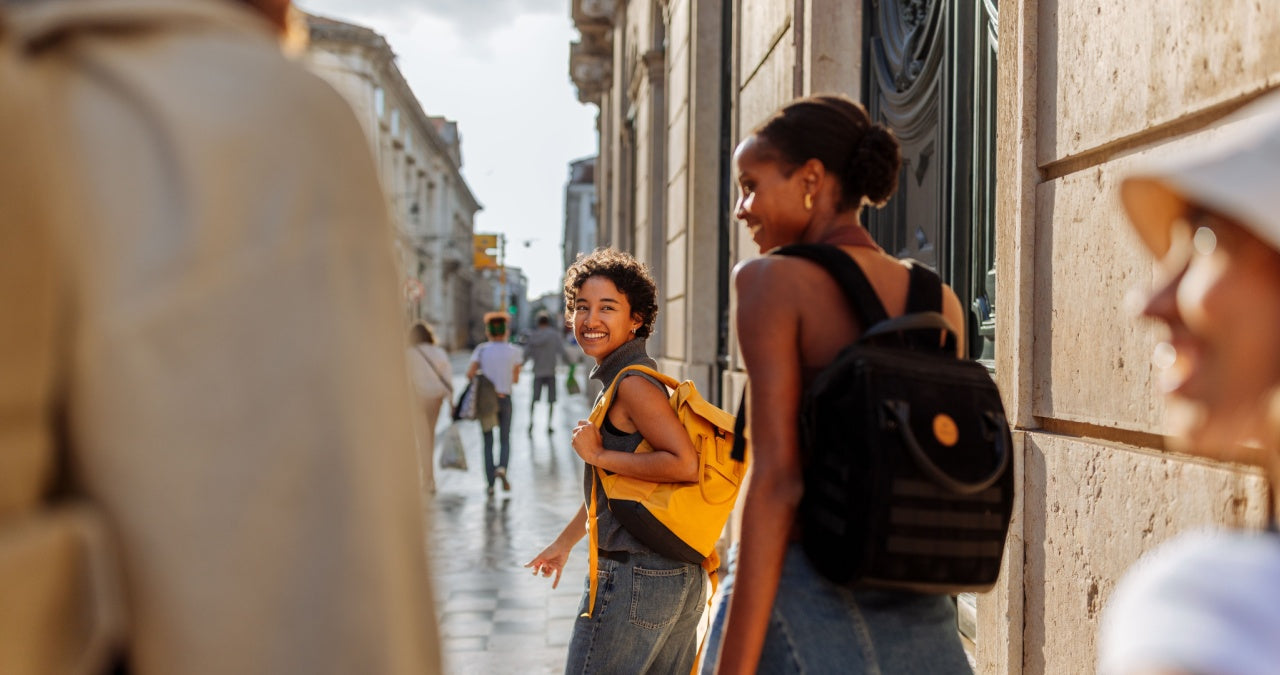 tefl grads walking down a city street, one with a yellow backpack and the other with a black backpack.